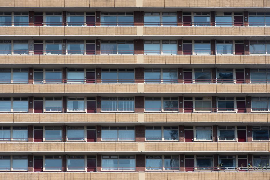 A multi-storey residential building with several concrete balconies featuring metal railings, some decorated with red and pink flower boxes. The building has large glass windows and a modern architect
